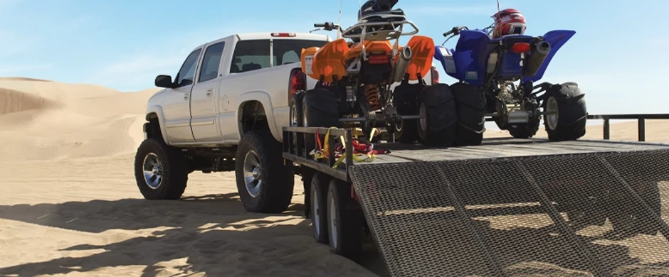 Truck, trailer, and all-terrain-vehicles amid vast sand dunes.