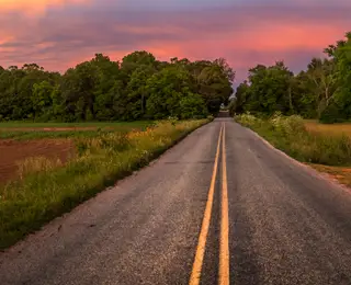 A two-lane road stretches forward past farmlands on a colorful spring day.