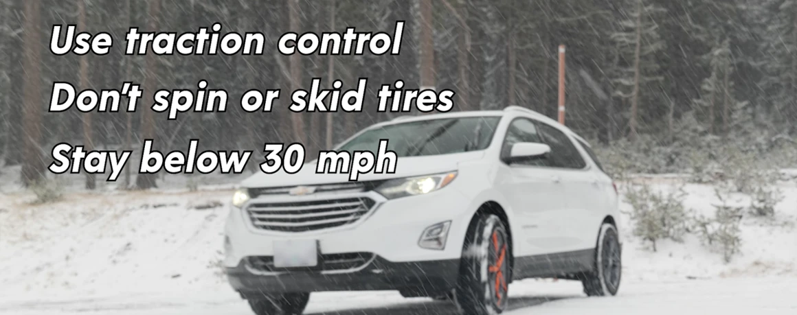 Car driving through snow with snow socks installed on the front drive wheels.