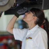 A Les Schwab technician stands undereath a vehicle up on a lift while examining a brake caliper. 