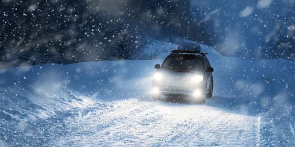 A car driving on a snowy highway at night.