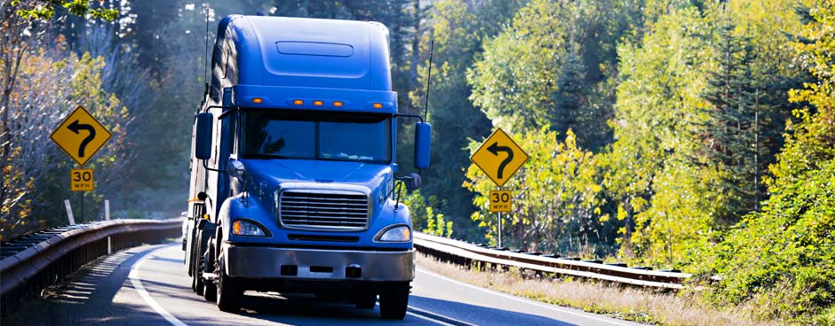 Royal blue semi-truck driving down forested highway.
